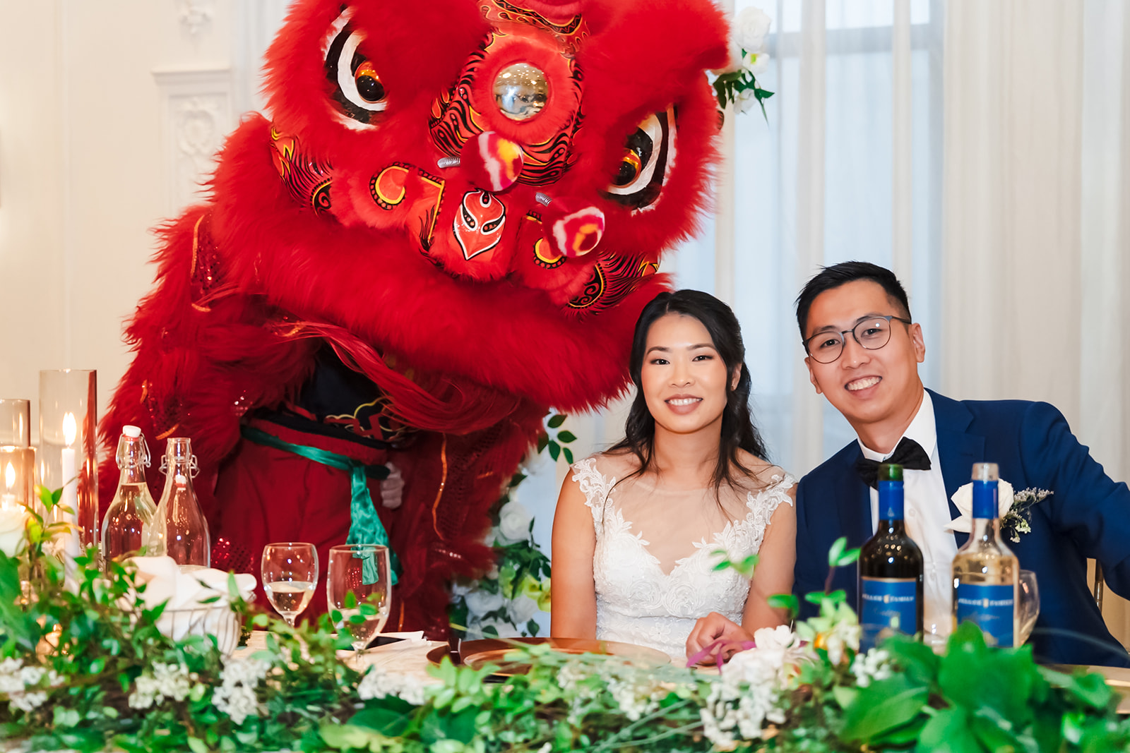 Monica and Andrew seated beside a red lion dance costume at their reception